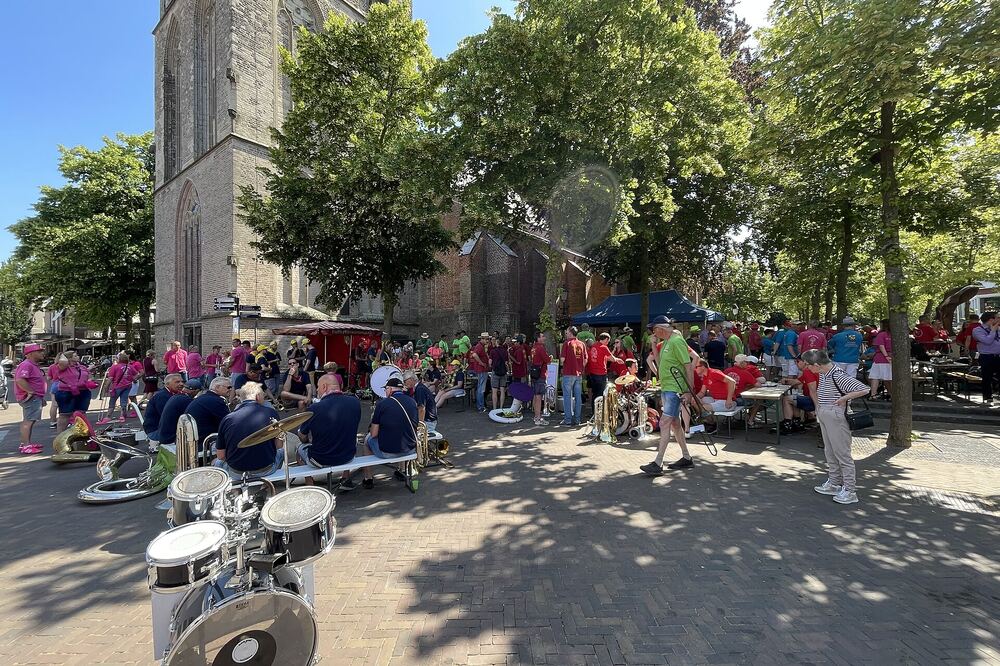 Een dweilorkest speelt op straat tijdens Ede Dweilstad, met de kerktoren erachter